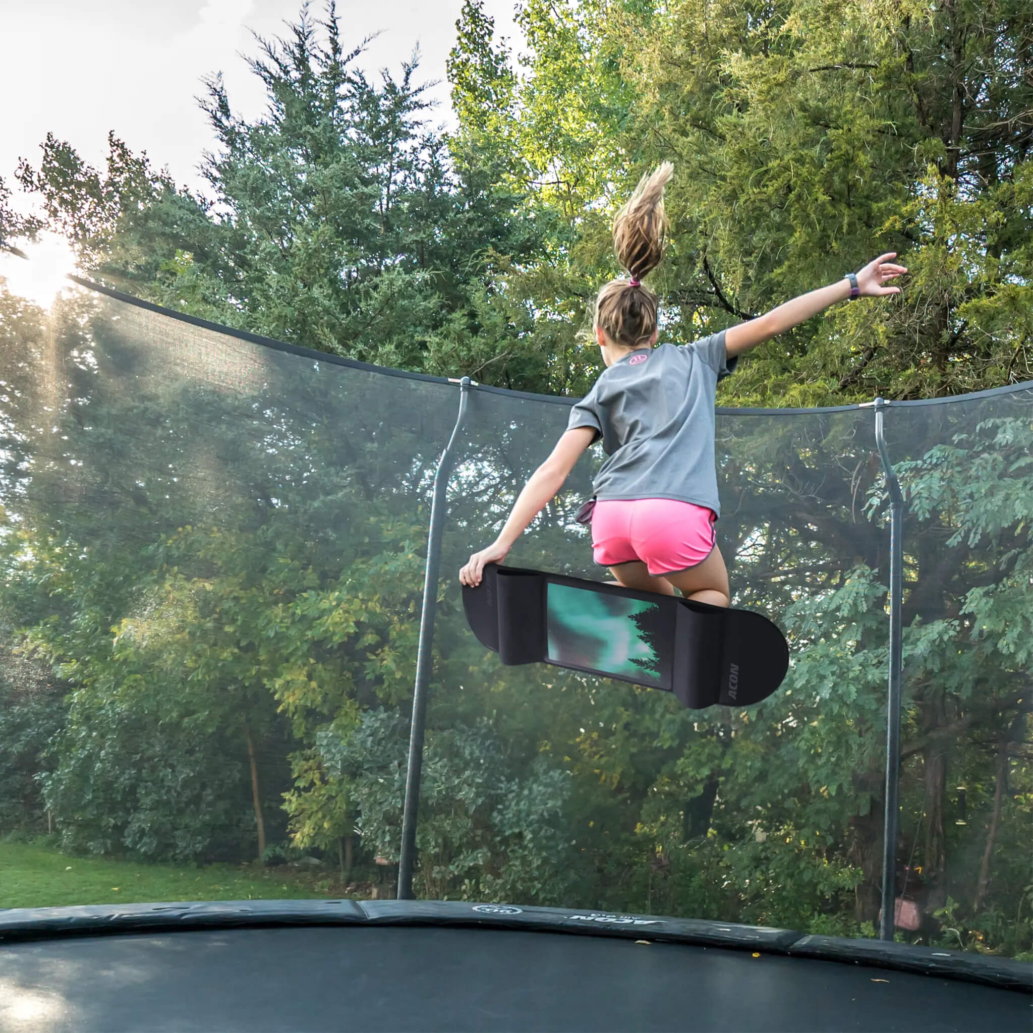 En flicka hoppar på en studsmatta med en Acon Skateboard till studsmatta.