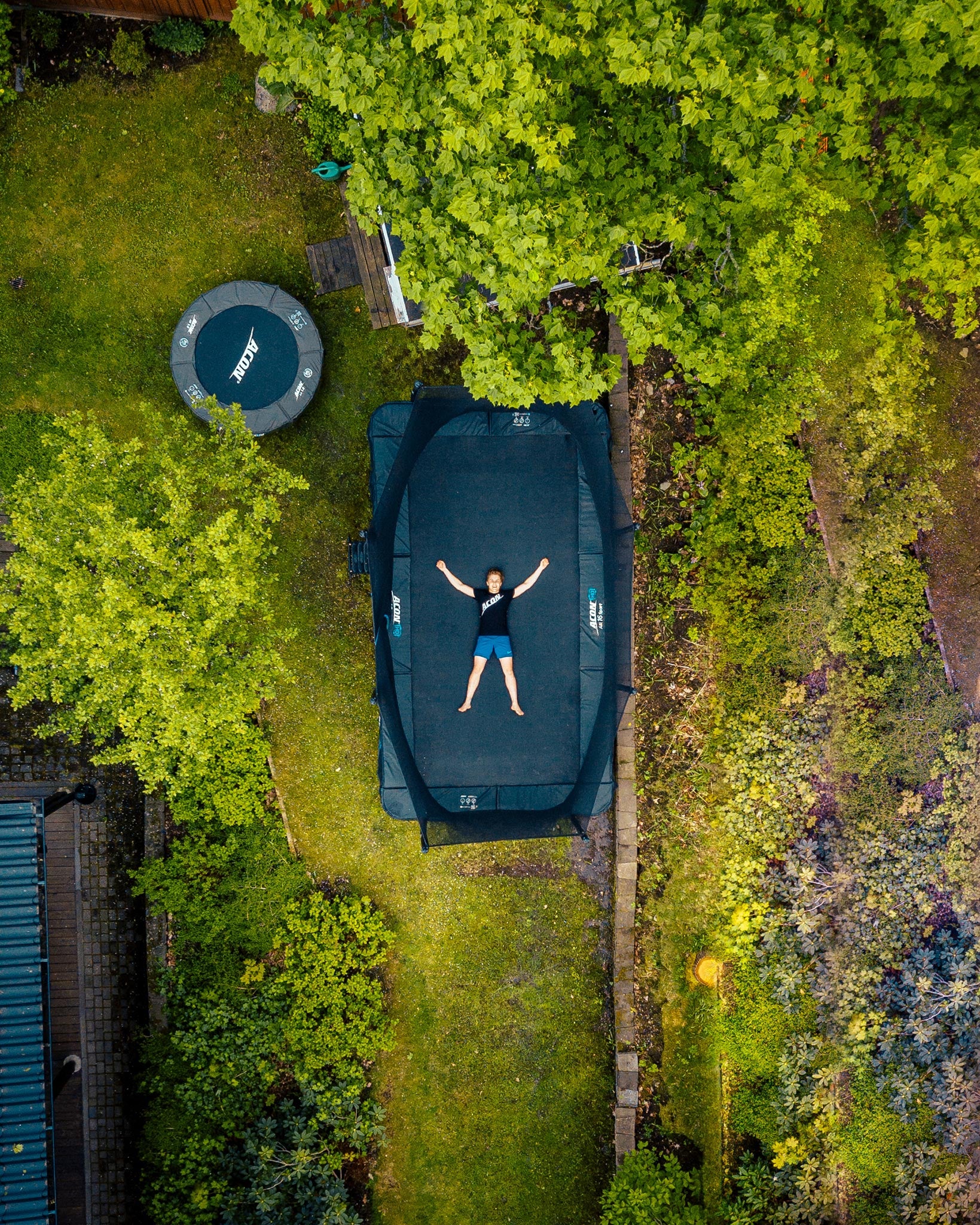 En pojke ligger på en HD-trampolin på en bakgård, sett ovanför