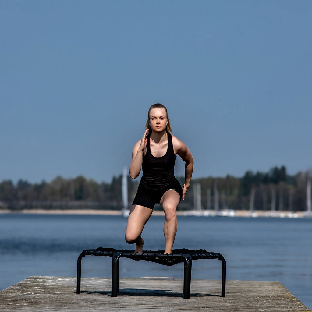 Tjej tränar utomhus på ACON FIT Hexagon trampolin vid sjön.