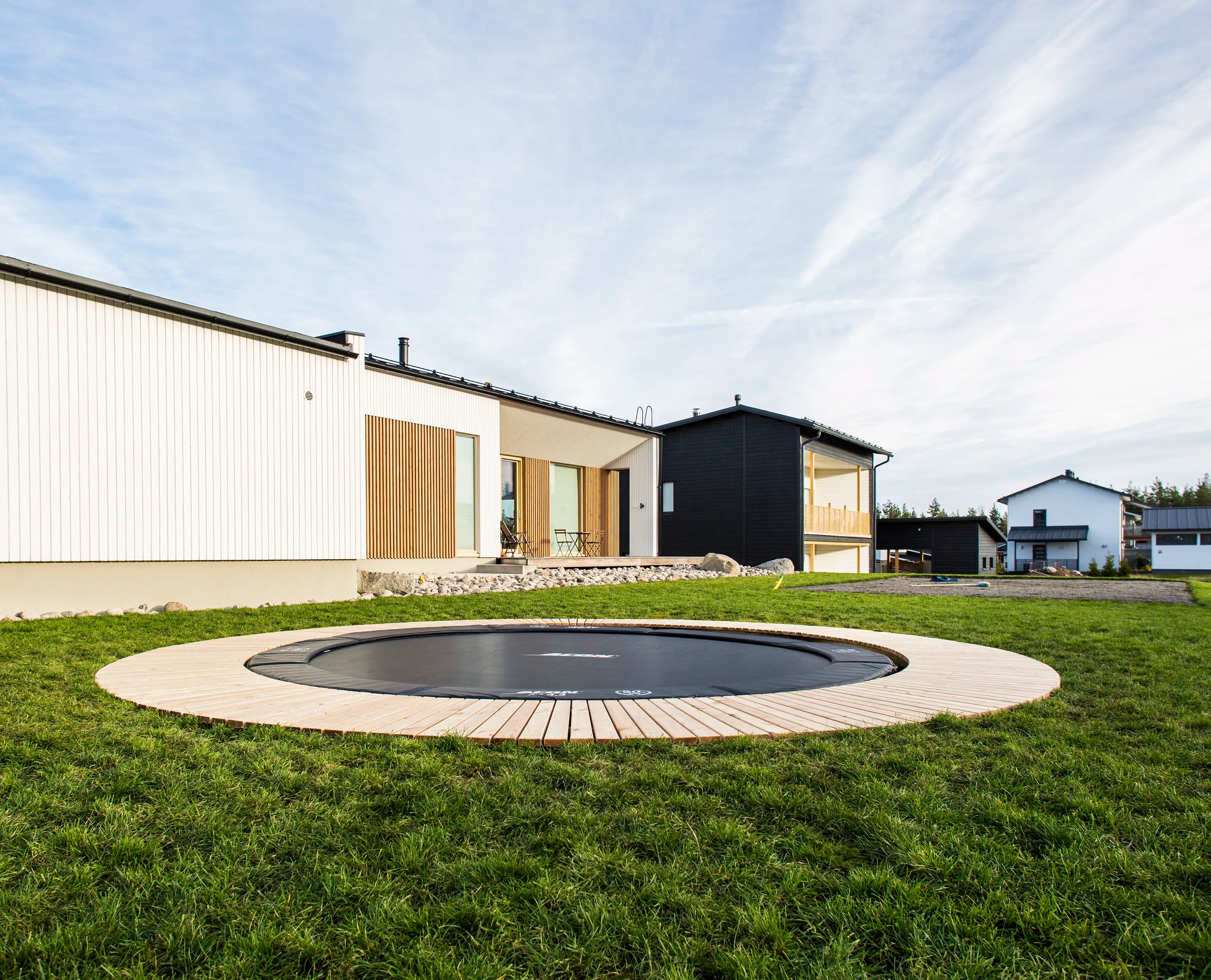 En rund trampolin av märket Acon installerad i marken. Omgiven av dekorativa träpaneler.